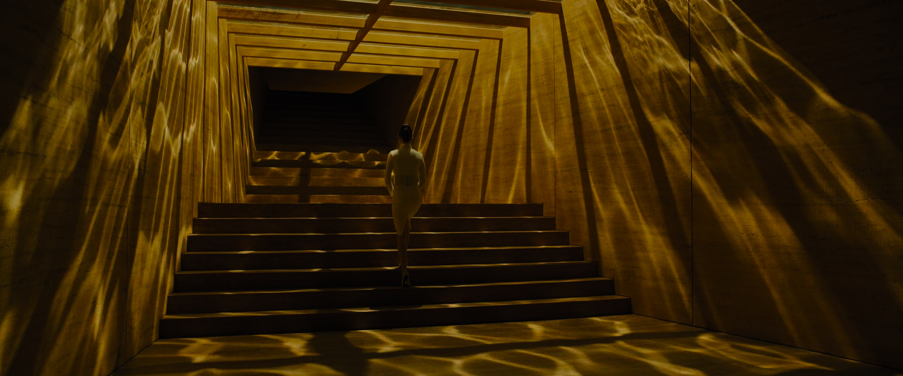 Luv-wearing-white-pencil-skirt-ascending-Wallace-Corp-staircase-basking-in-gold-light